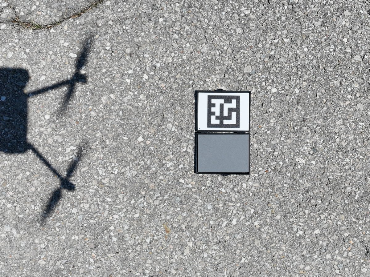 A calibrated reflectance panel on the ground, photographed from a drone whose shadow falls beside it