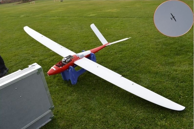 Fixed-wing UAV carrying a hyperspectral imager on a grass field, with an inset of the aircraft in flight