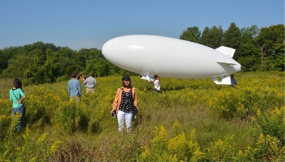 A research blimp over a grassland field site, with the team in the tall grass
